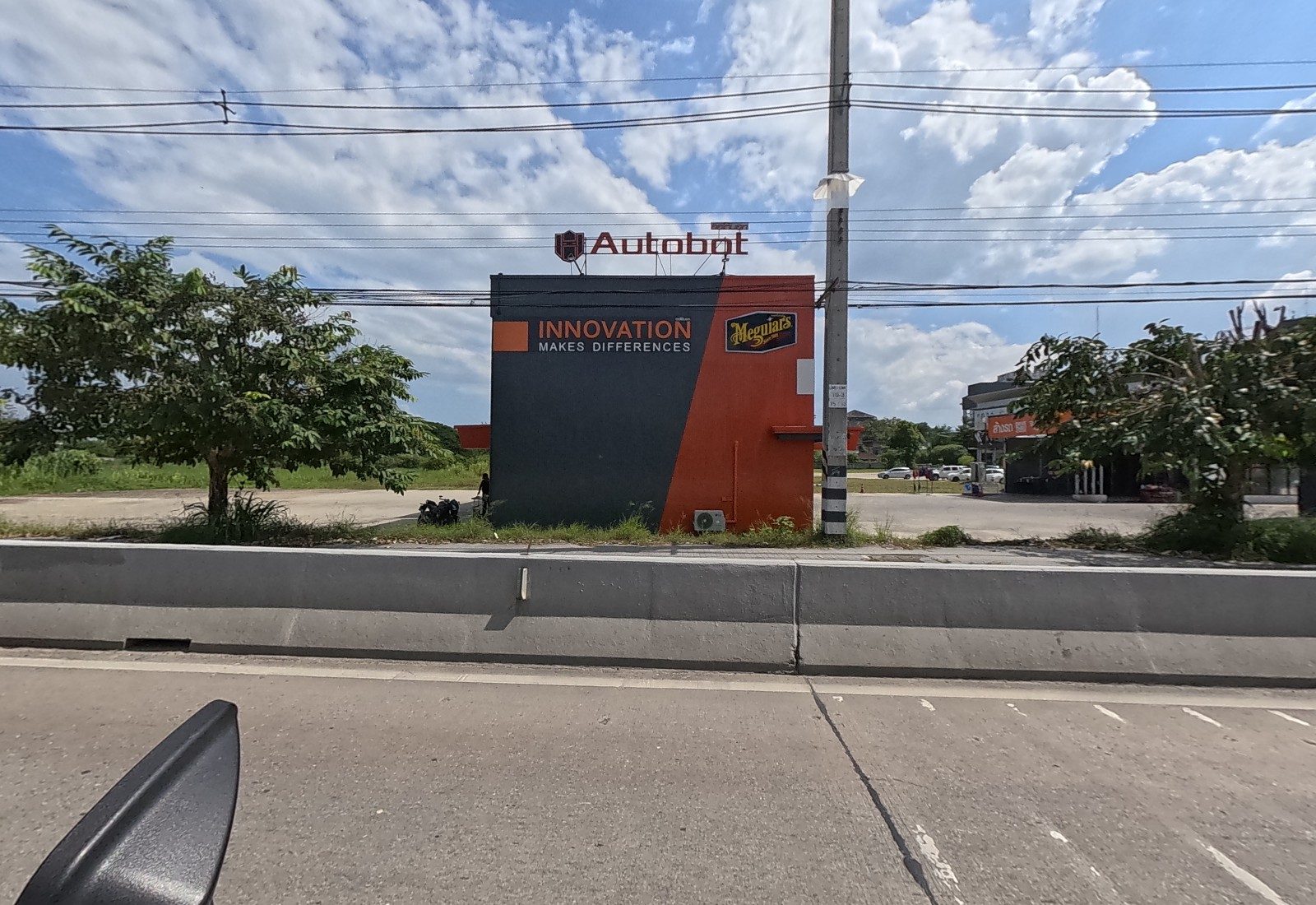 Back at ground level: an Autobot car-care kiosk in orange and charcoal on open land, with a car-wash building behind.