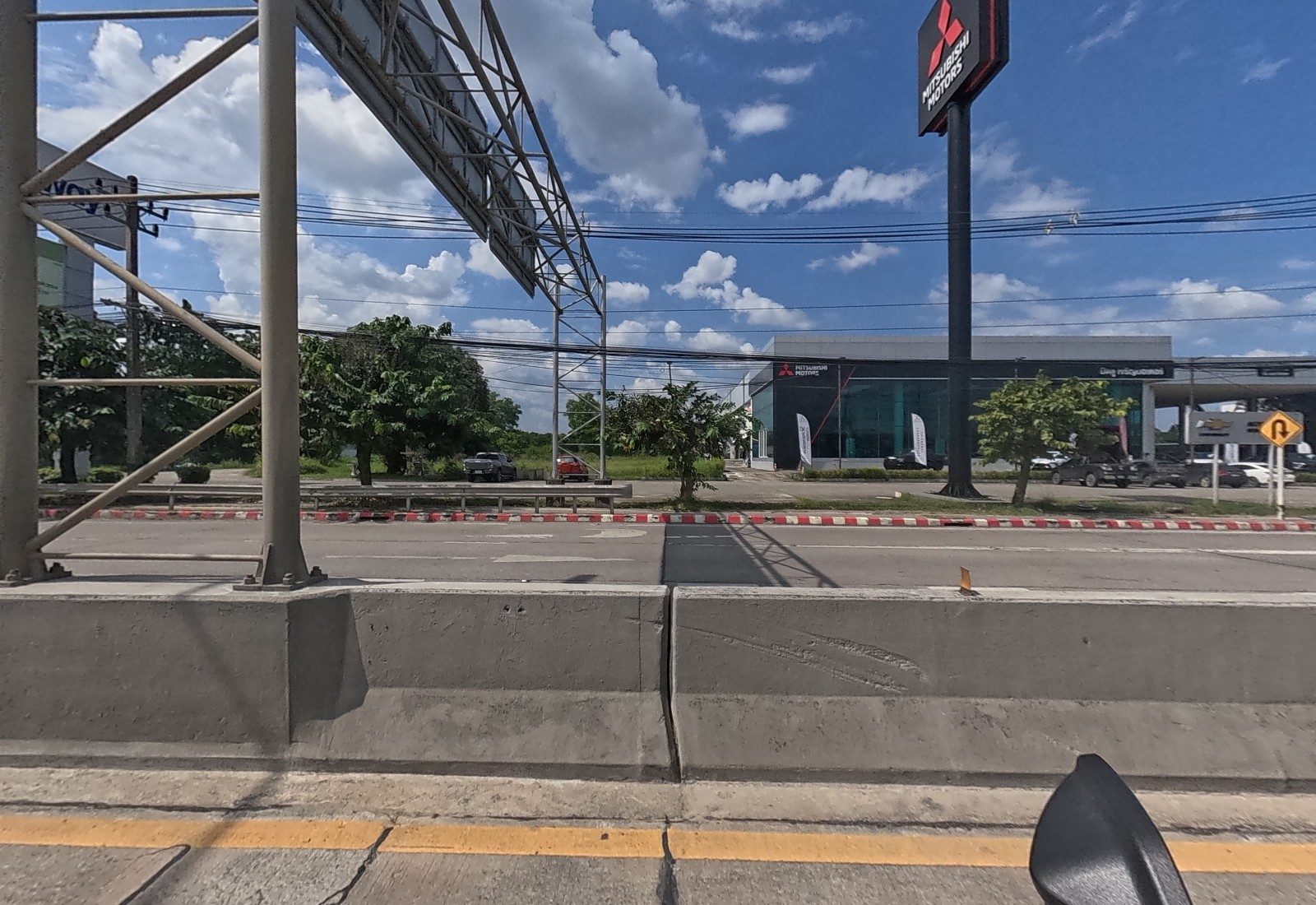Across the road beyond a sign gantry, the Mitsubishi Motors showroom with its pylon, a Chevrolet service sign and a U-turn sign.