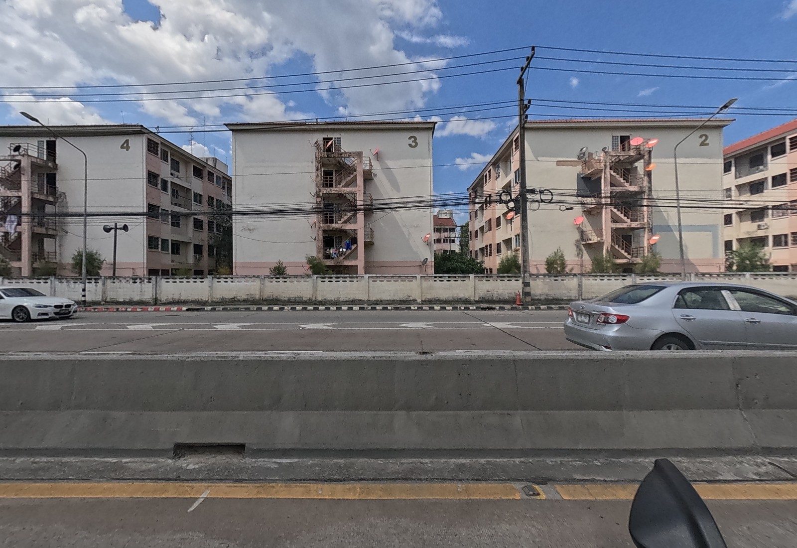 Across the median, Baan Ua Arthorn blocks 4, 3 and 2 stand in a row behind a wall.