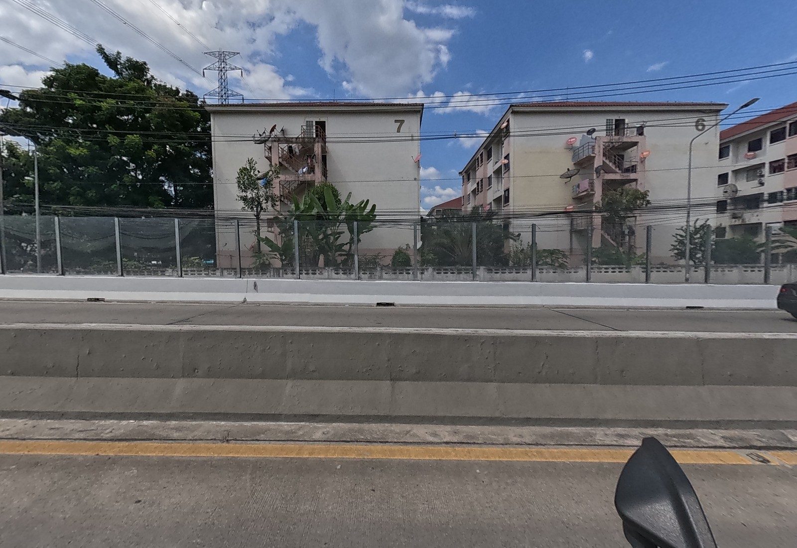 Across the flyover, two four-storey public-housing blocks painted with the numbers 7 and 6 behind a mesh fence.