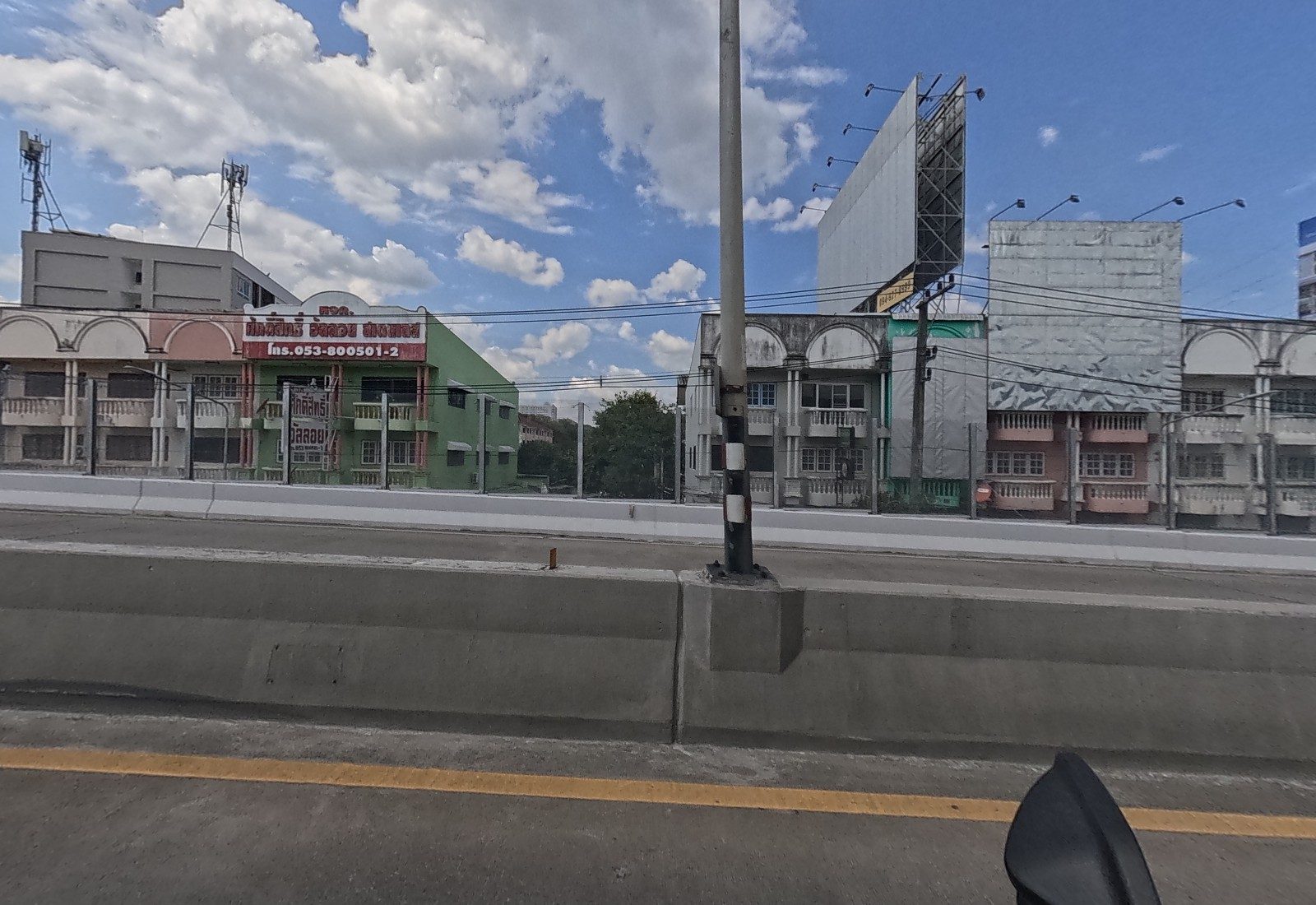 Across the flyover, a green shophouse with a red sign for a stainless-steel and alloy firm, then blank billboard frames and old arcaded shophouses.