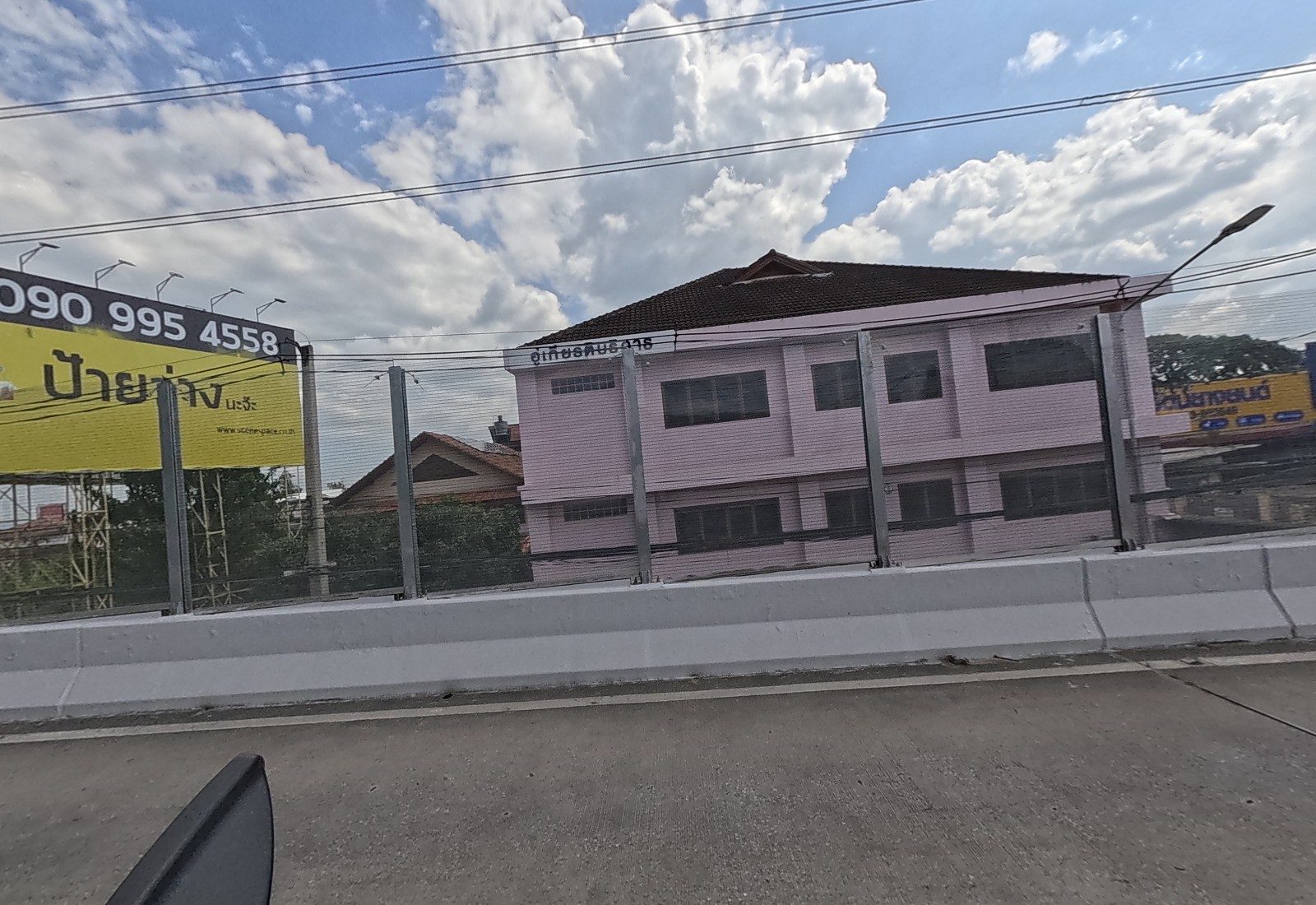 Below the flyover, a pink two-storey building signed as a garage, beside a yellow billboard, with a tyre-shop sign further on.