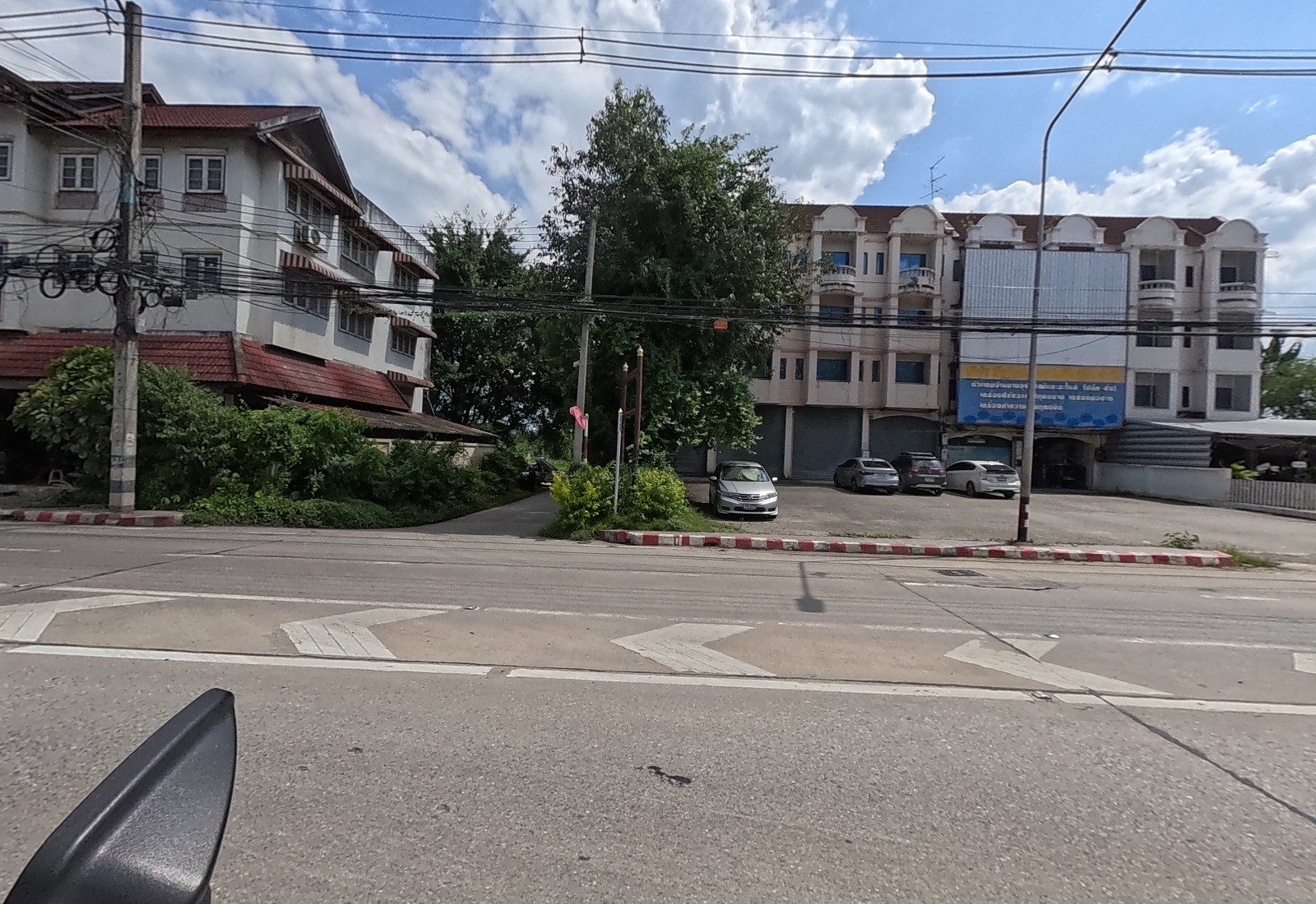 At ground level: a soi mouth between a tree and a shophouse block with a blue refrigeration-parts sign and cars parked in front.