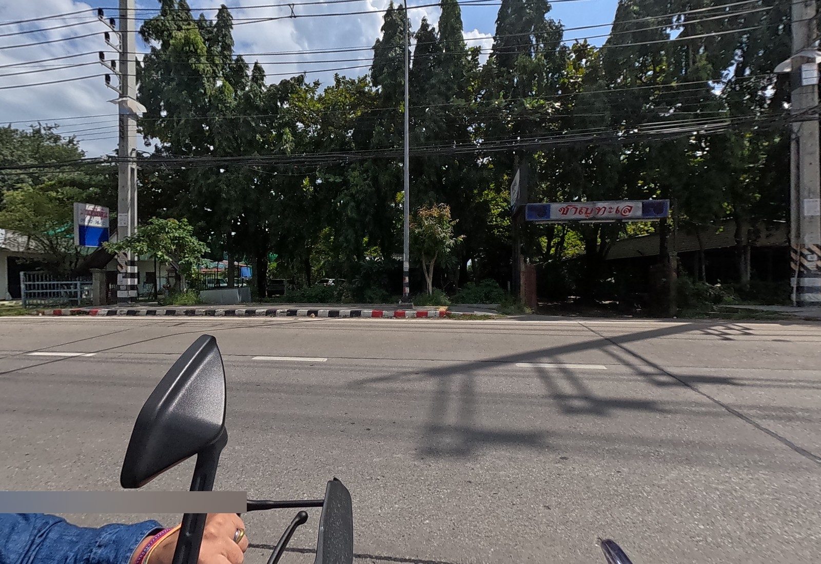 Tall trees with a gate sign for a seafood restaurant and a small blue-and-white shop sign by a gate; the rider's hand and mirror in the foreground.