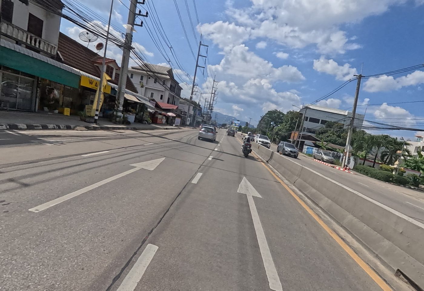 Main road ahead with shopfronts on the left and hills in the distance