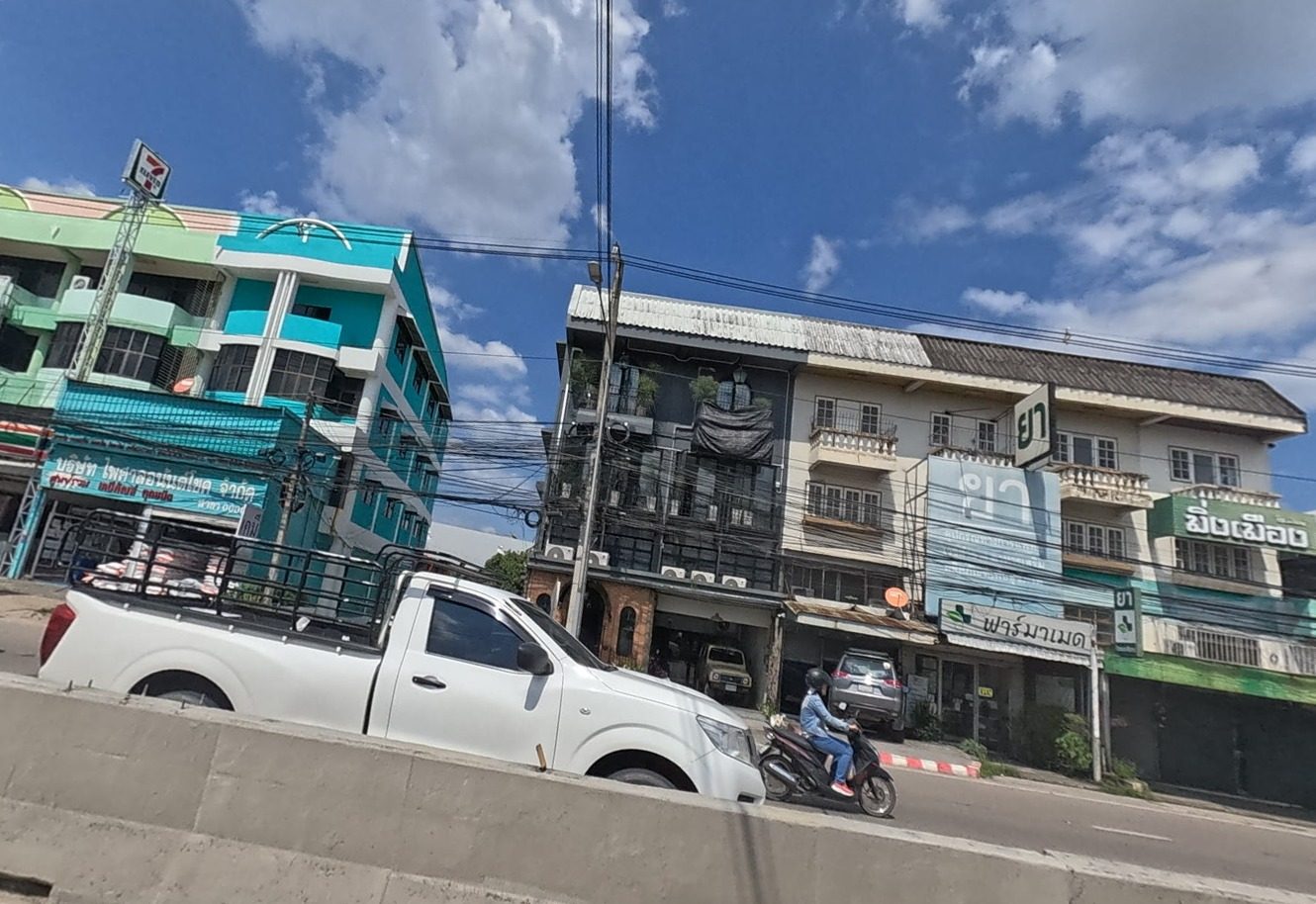 Row of shophouses with a 7-Eleven, a pharmacy and a supply shop along the main road