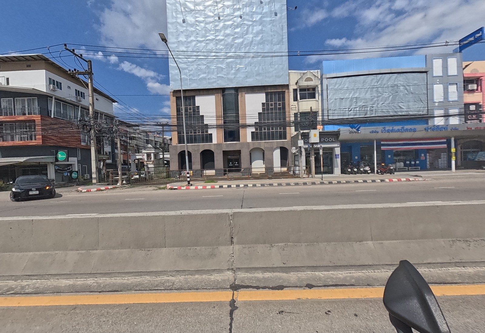 Across the road, a brown modern building with a green round logo, a silver-clad tower, the World Pool / World Chemical shopfront with a Thai flag.