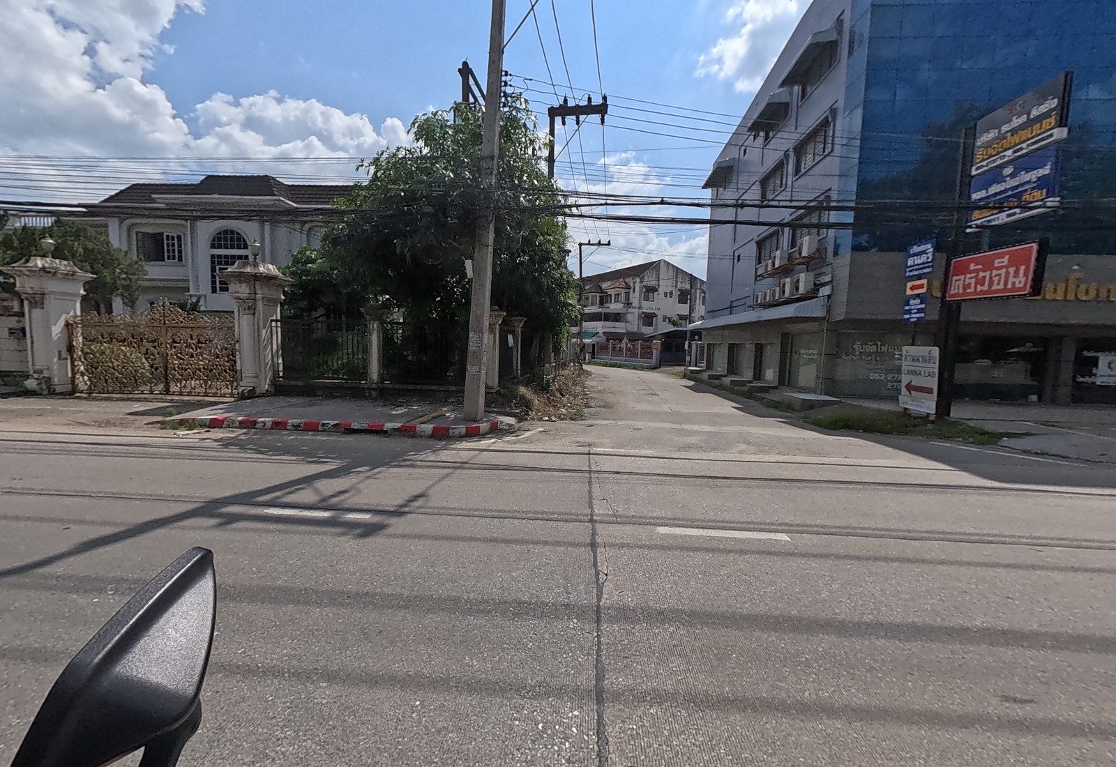 A soi opens between a gated mansion and a blue-glass building carrying a red 'ครัวจีน' sign, a leasing company fascia and a Lanna Lab arrow.