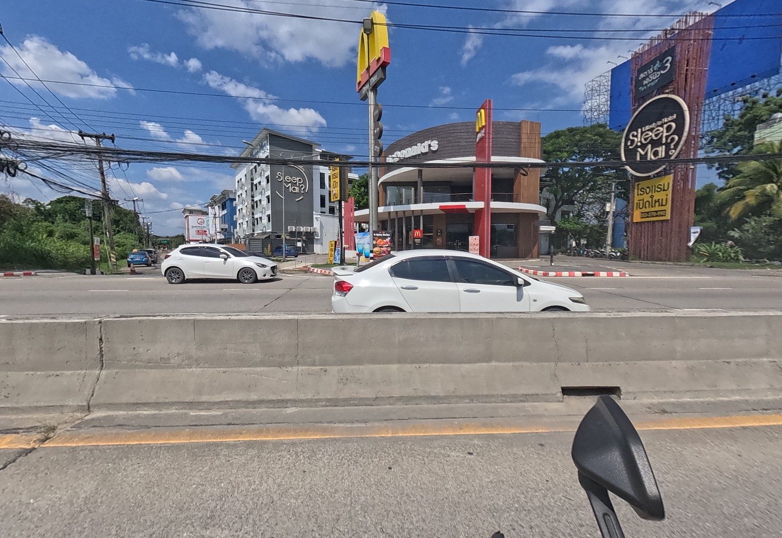 Across the median, McDonald's, the grey Sleep Mai hotel building and the Sleep Mai tower sign stand side by side.