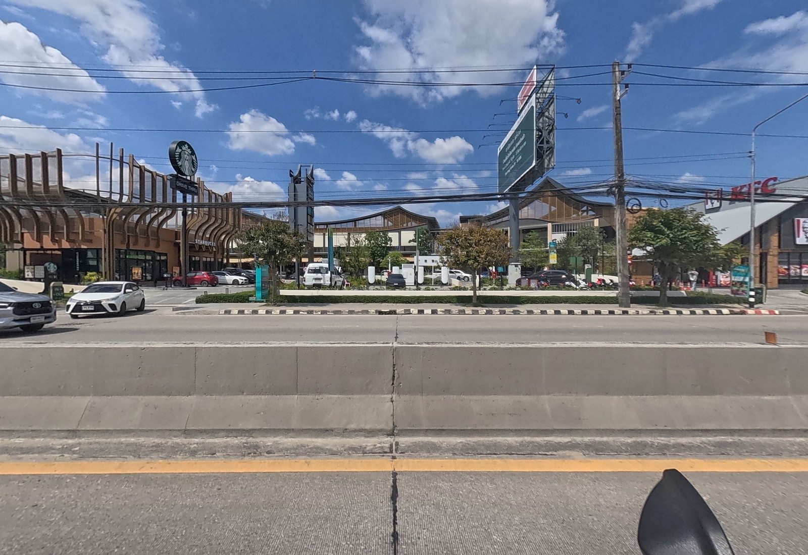 Across the median, the timber-clad Backyard mall holds a Starbucks drive-thru and a KFC, with EV chargers and a car park in front.