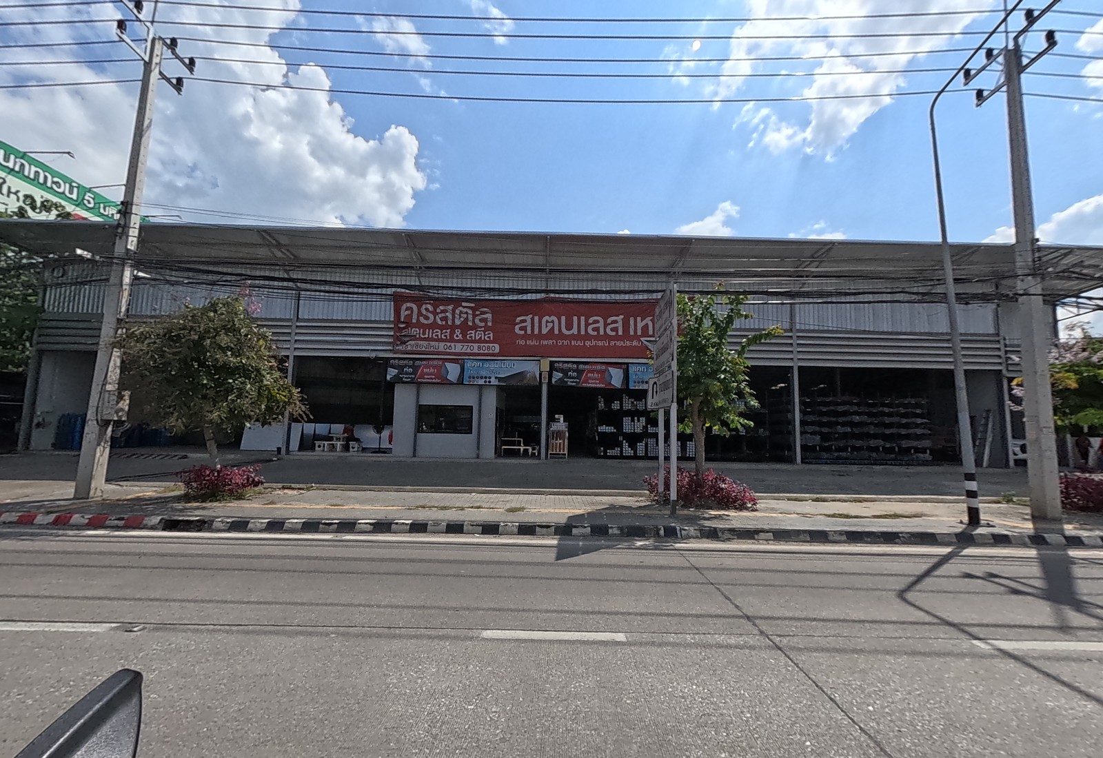 A long steel-roofed warehouse shop with a red banner for Crystal Stainless & Steel, racks of steel sections inside and a U-turn sign on the kerb.