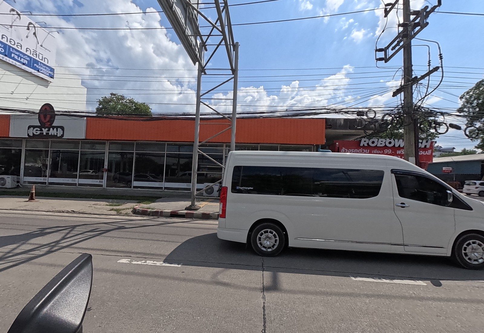 The O2 Gym under an orange roof and the Robowash car wash, with a white van passing and a clinic billboard at top left.