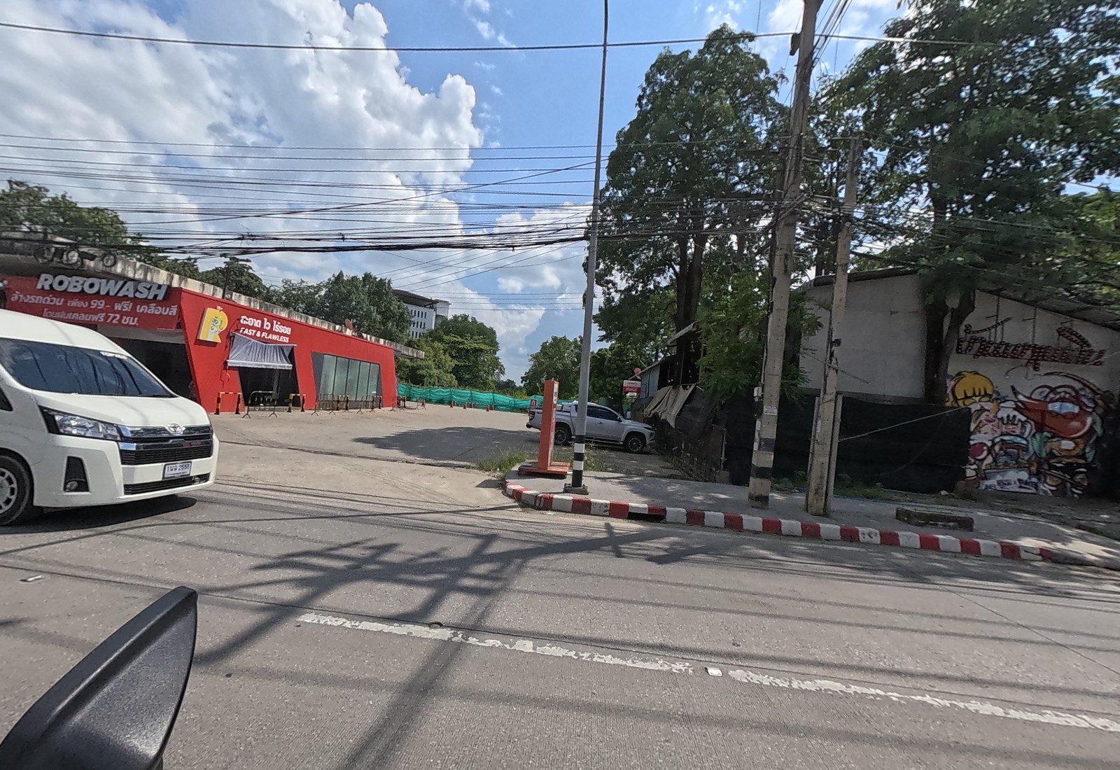The red Robowash car wash with its forecourt, a side lane, and an old shed covered in a big graffiti mural under trees.