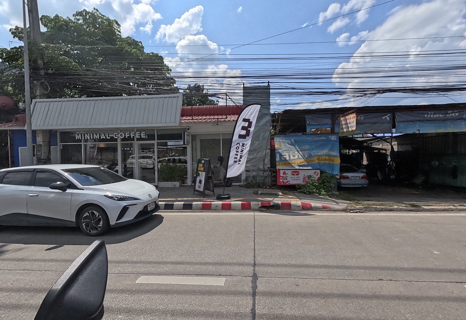 MINIMAL COFFEE with a flag banner and an A-board; next door an open garage behind a faded phone-shop banner.