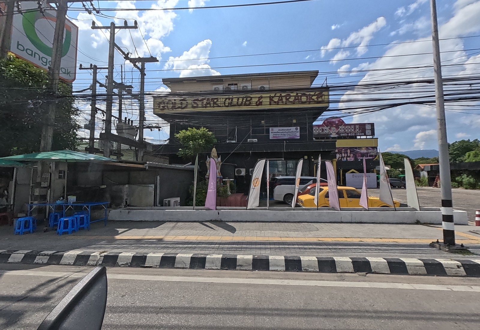 The GOLD STAR CLUB & KARAOKE building with flag banners and a spirit house out front, a street-food stall with blue stools beside it, and a ROCK & ROLL billboard.