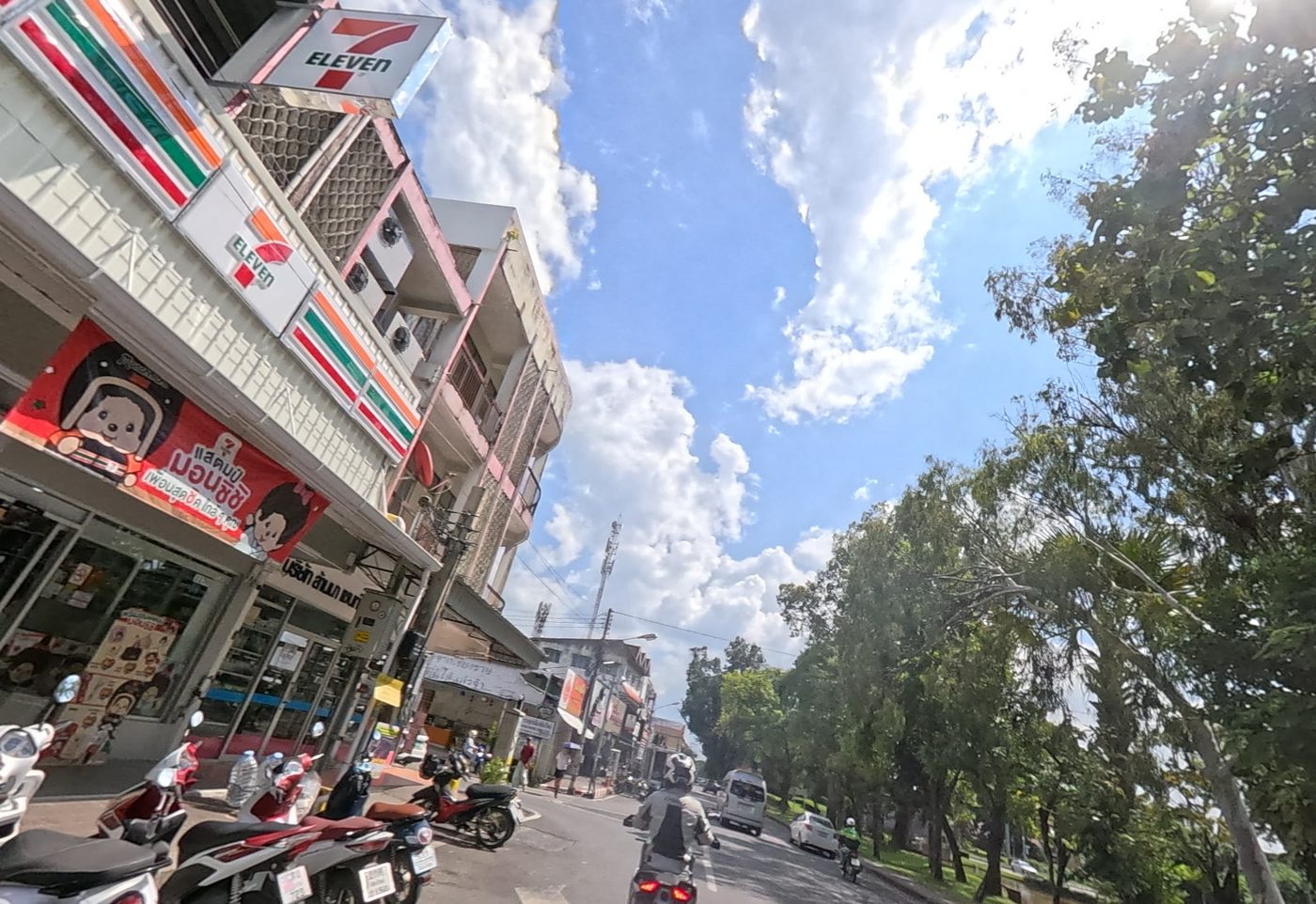 Old-city street corner with a 7-Eleven and parked motorbikes