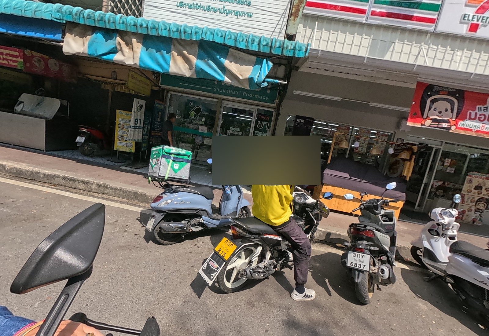 A Maxim rider in a yellow vest and a LINE MAN scooter park in front of the คณายา pharmacy and a 7-Eleven.