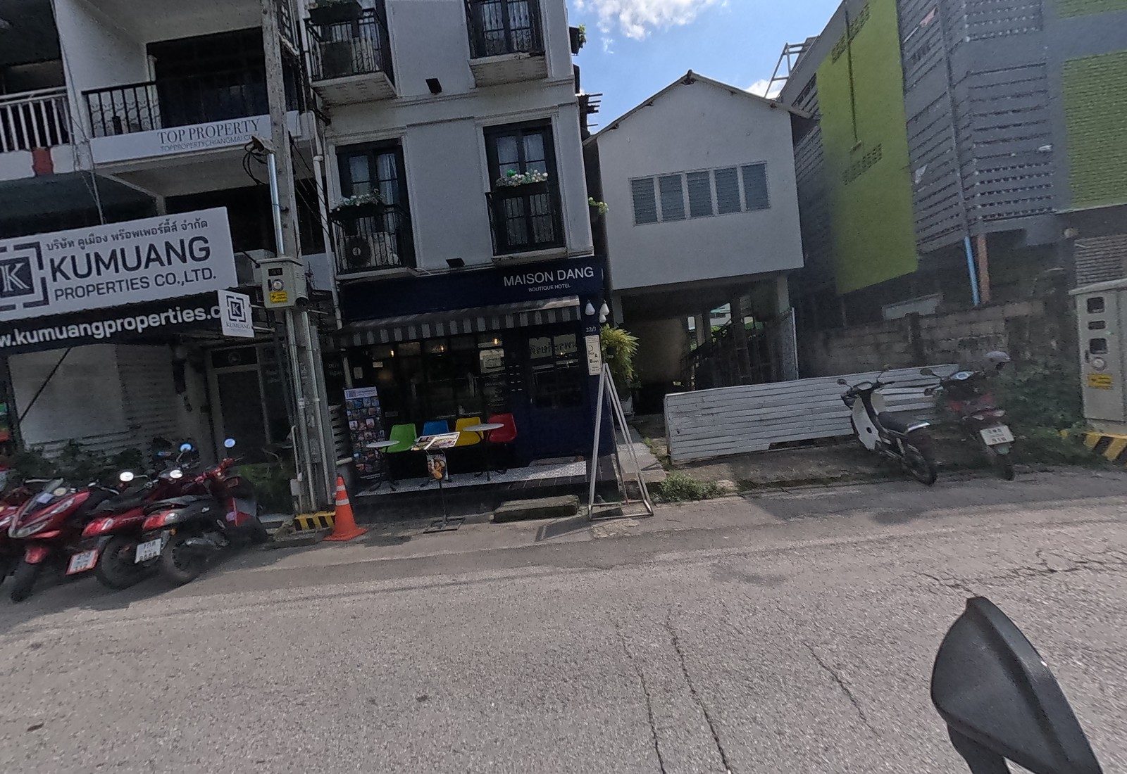 Maison Dang Boutique Hotel at 22/1 has colourful chairs out front, beside the Kumuang Properties and Top Property offices; motorbikes park along the kerb.