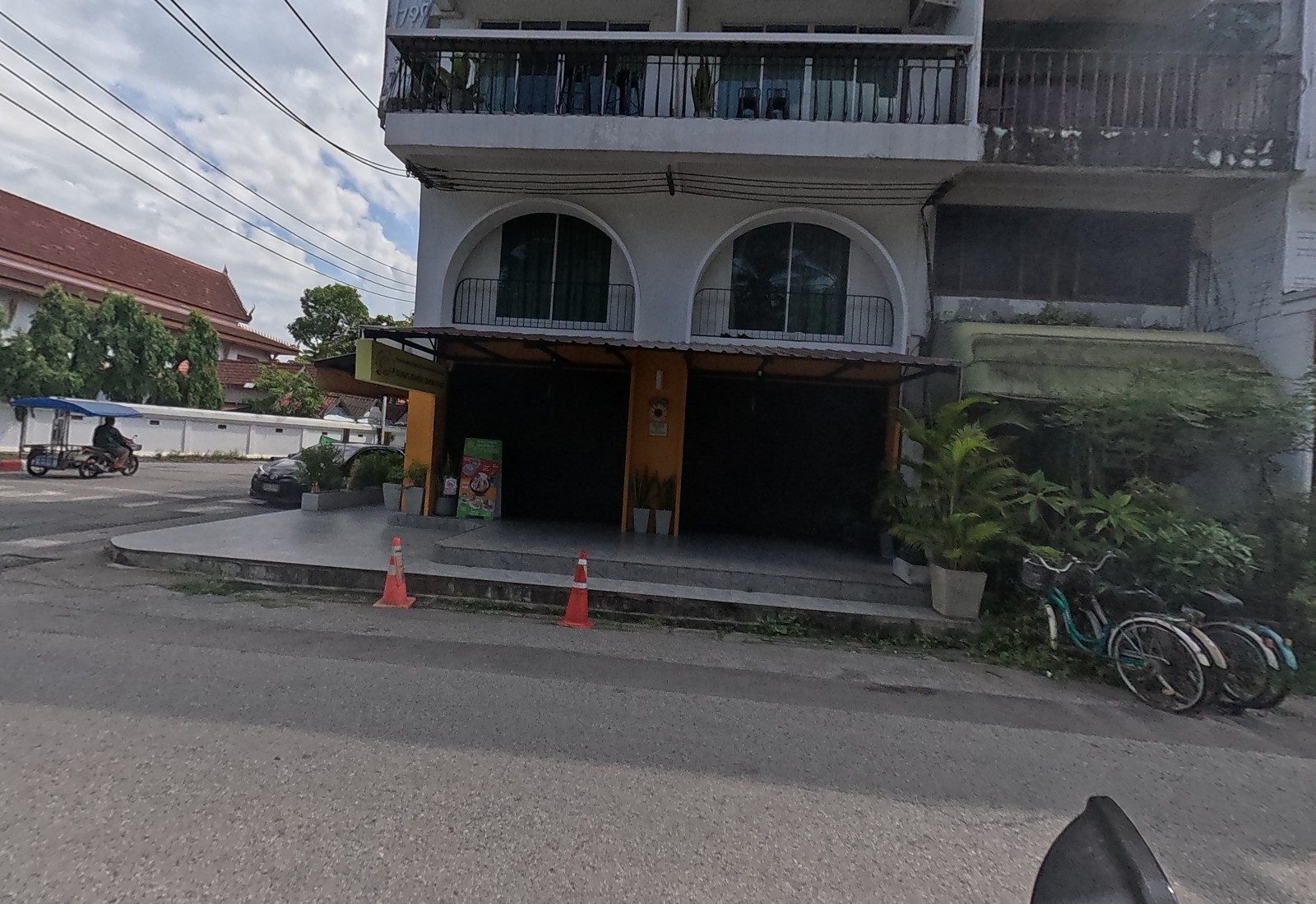 A white arched corner building with orange pillars houses Sunflower Smoothie, its menu board out front and traffic cones on the step; bicycles lean on the right.