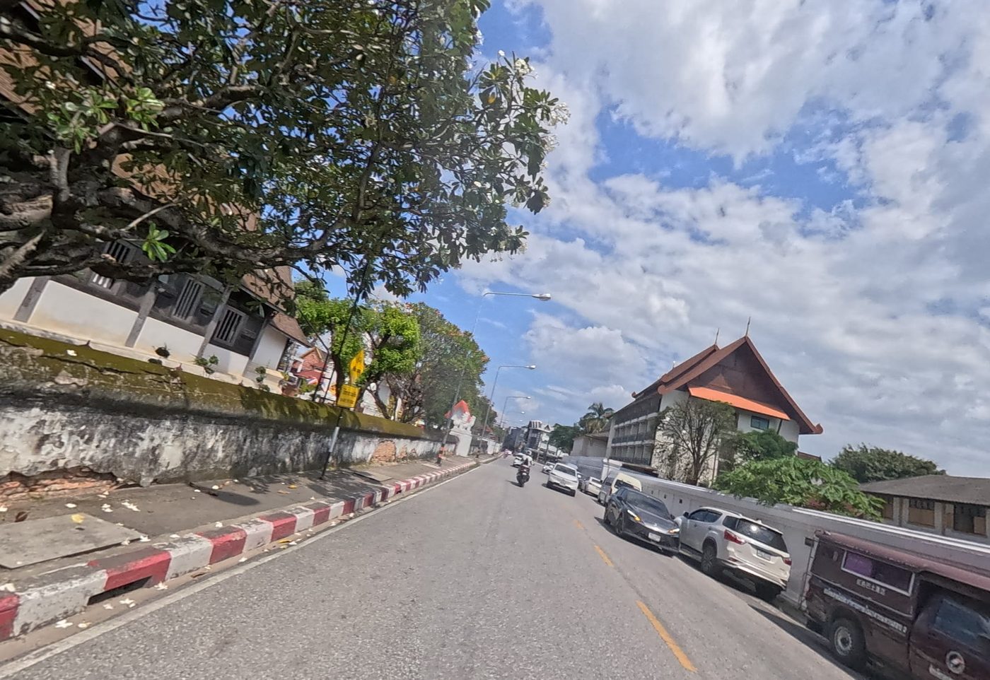Old-city lane beside an old brick wall, with a wat building ahead
