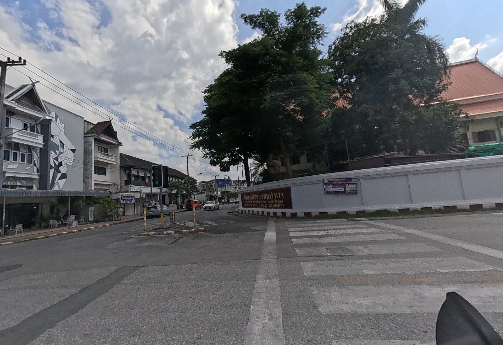 Wat Phra Singh's name board reads วัดพระสิงห์ วรมหาวิหาร, WAT PHRA SINGH A.MUANG CHIANGMAI, on the curved white wall; a purple notice mentions ตำบลพระสิงห์; the August Hostel's lion mural is at left.