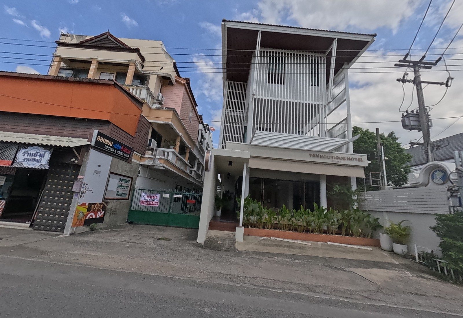 Ten Boutique Hotel's white slatted three-storey front stands beside a gated lane with a ให้เช่า FOR RENT sign and the orange ออกแบบ-ผลิตสิ่งพิมพ์ DESIGN & PRINT SHOP.
