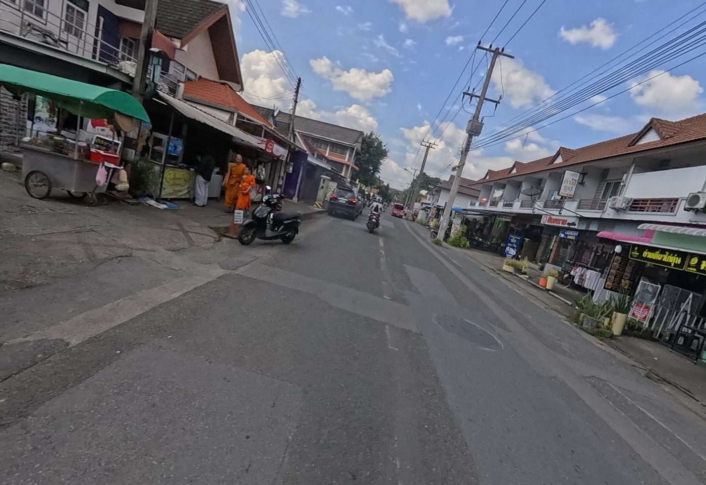 Shophouse street with a food cart and monks on the pavement