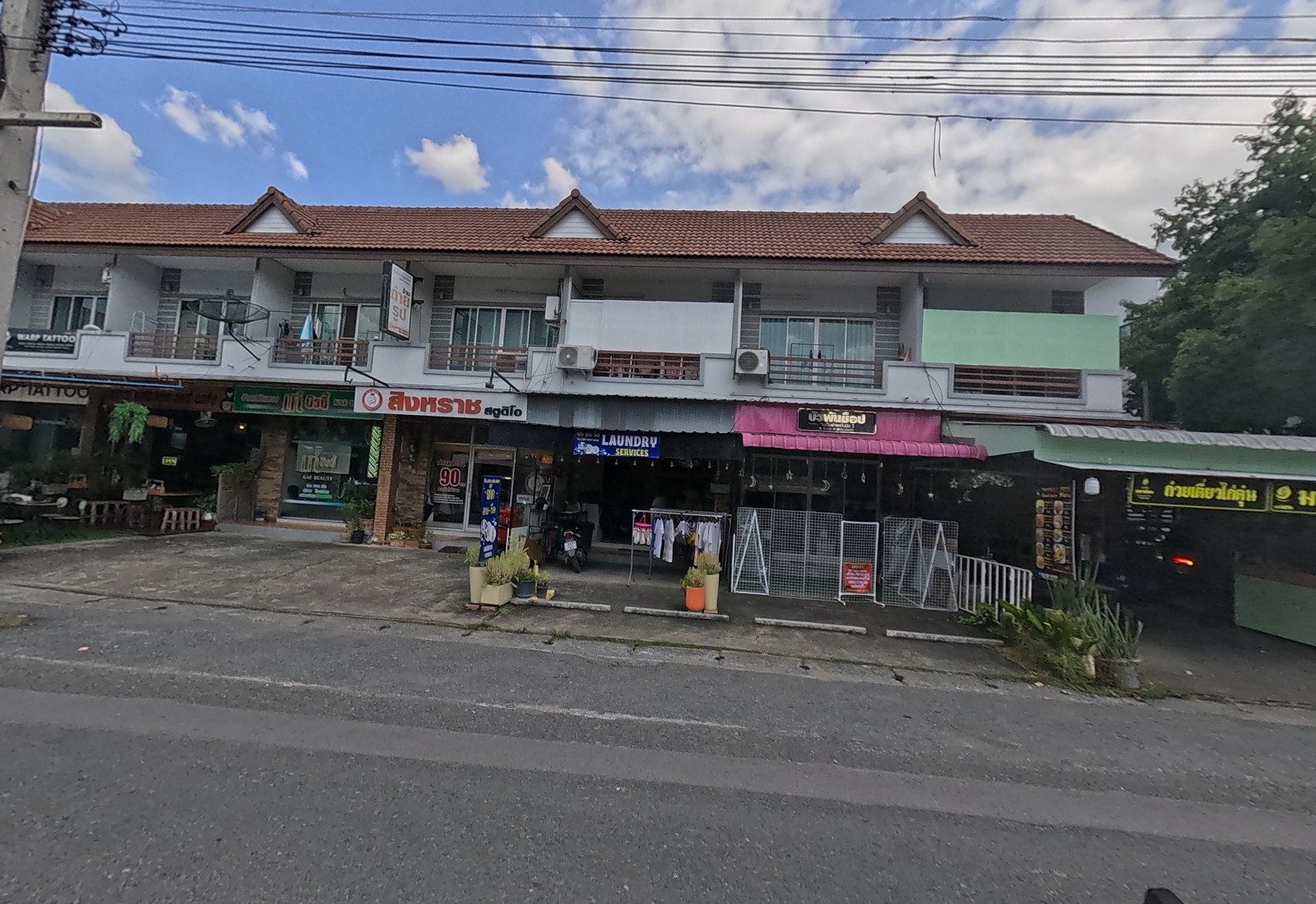 A two-storey shophouse row: Warp Tattoo, Kae Beauty, Singharat Studio, a laundry, a pink-awninged shop and the Maha Niyom noodle shop.