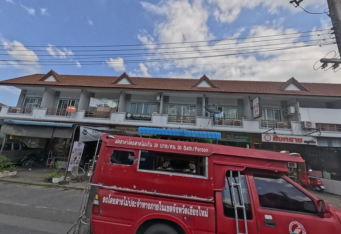 Red songthaew shared taxi passing a row of two-storey shophouses