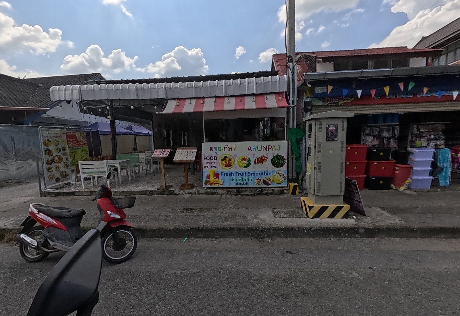 Arunpaj's open-front food and smoothie shop with white seating and menu stands, a household-goods shop next door.