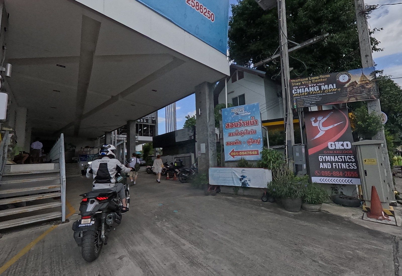 Riding in under the building; at the corner stand the Krupayu Swim sign, the Chiang Mai Muay Thai Gym visa sign and the GKO gymnastics sign.
