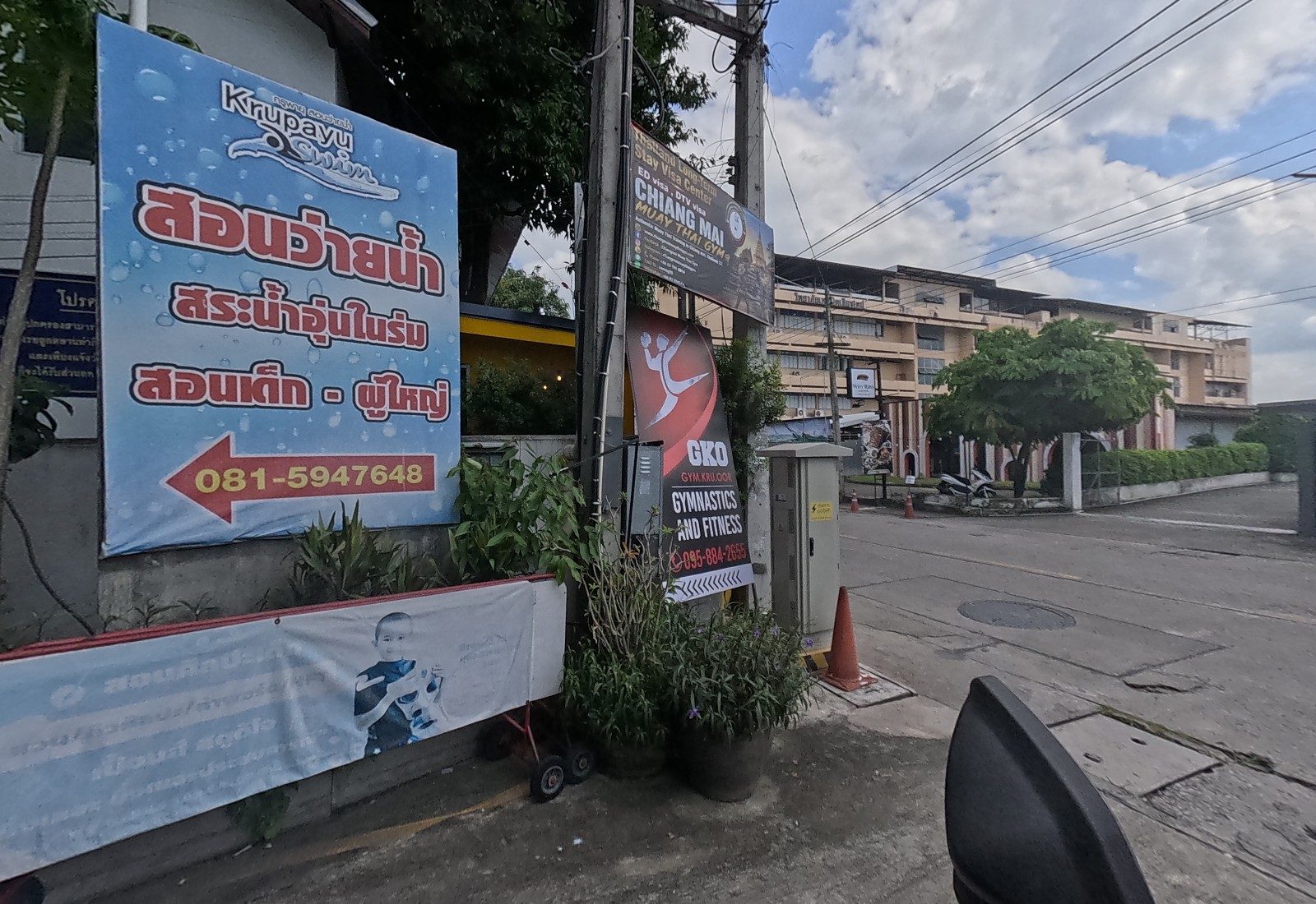 Close view of the Krupayu Swim sign with the GKO gymnastics sign and the Chiang Mai Muay Thai Gym sign on the pole beside it.