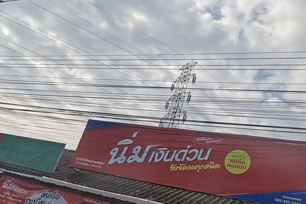A fast-loan and vehicle-registration shop with a big red sign and phone number sits beside a noodle-shop food cart and motorbikes parked under an awning.