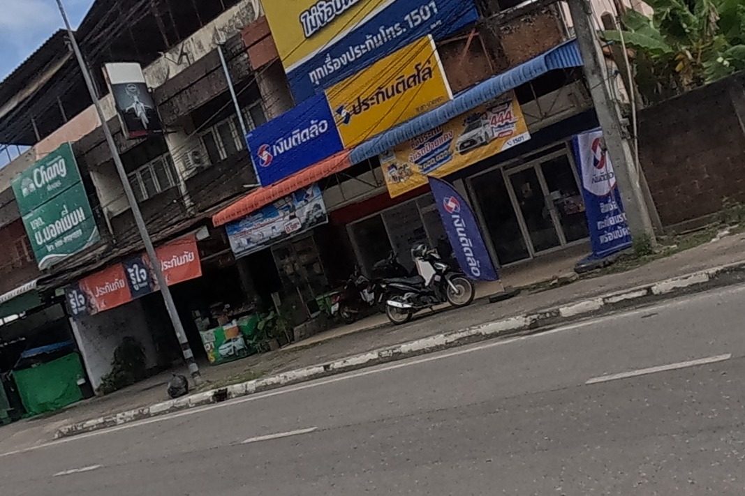 A vehicle-title loan branch called Ngern Tid Lor sits among shops with insurance signage, a 10-month 0%-instalment billboard above, banana trees behind a brick wall further along.