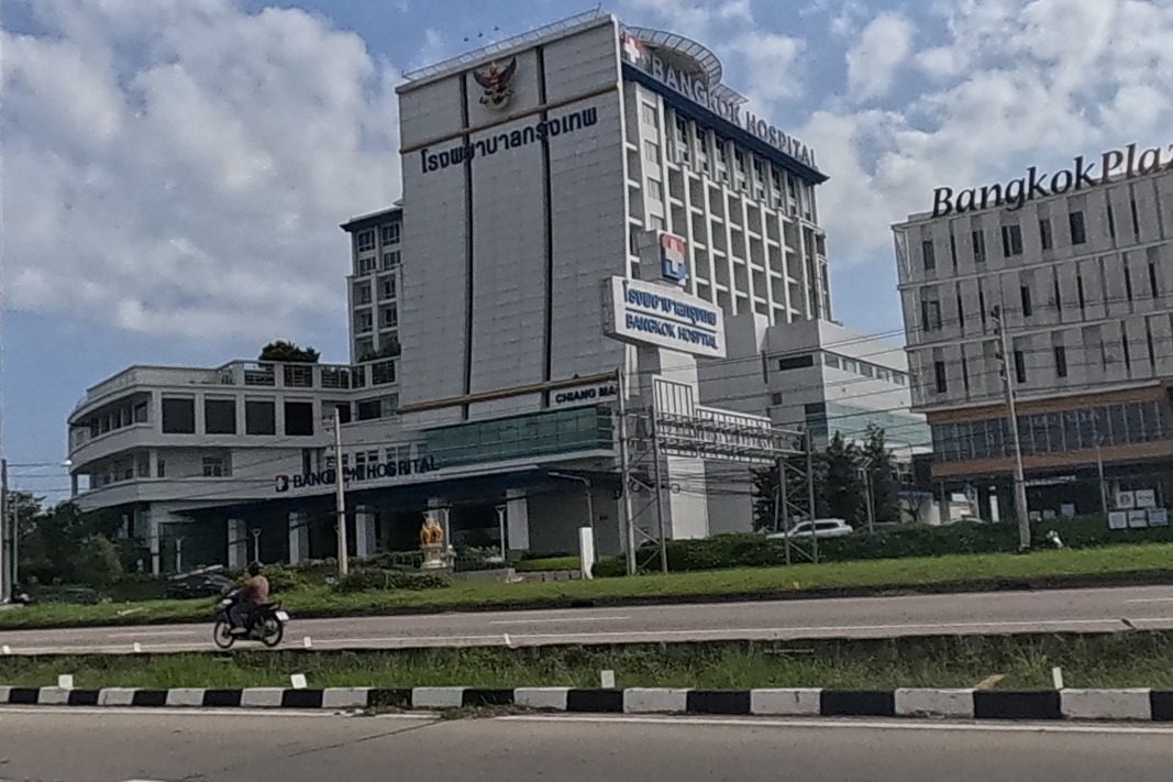 Bangkok Hospital Chiang Mai and Bangkok Plaza 2 are both clearly signed across the road, with a motorcyclist passing on the median.