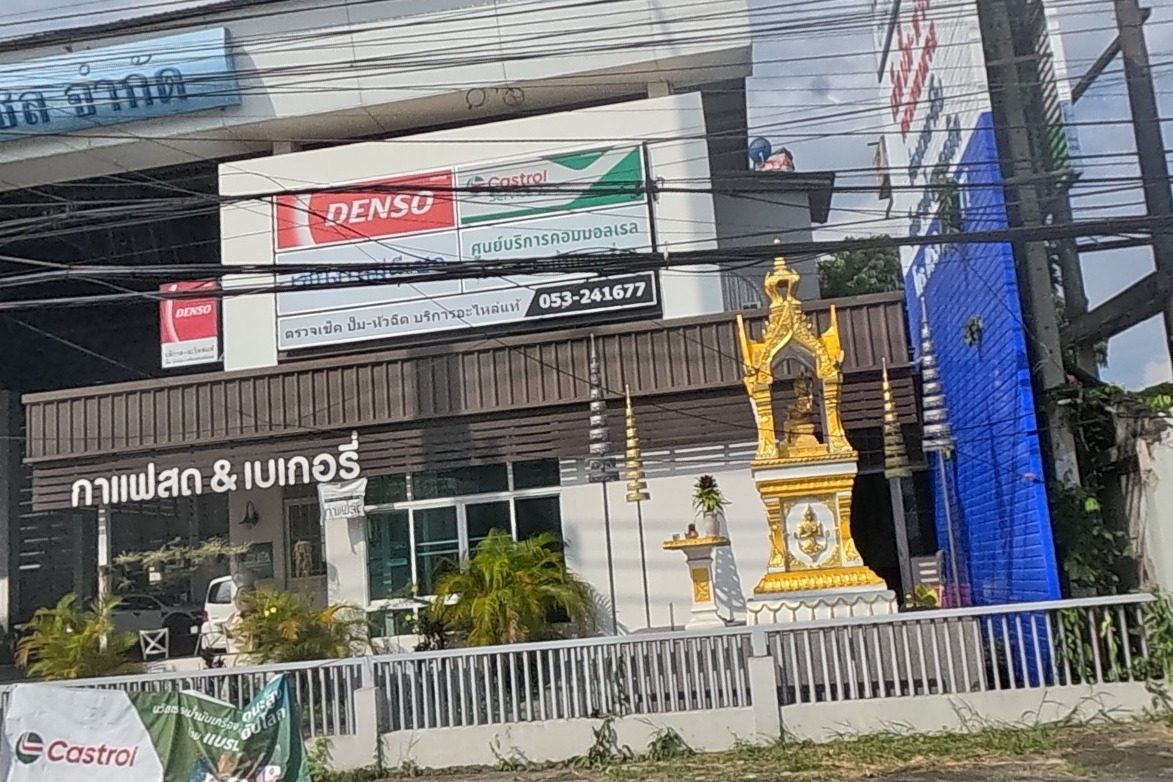 A DENSO/Castrol common-rail diesel service shop (part of the VW/Audi/Seat/Skoda repair garage) has a phone number and a large ornate gold spirit house out front, next to a fresh coffee and bakery shop.
