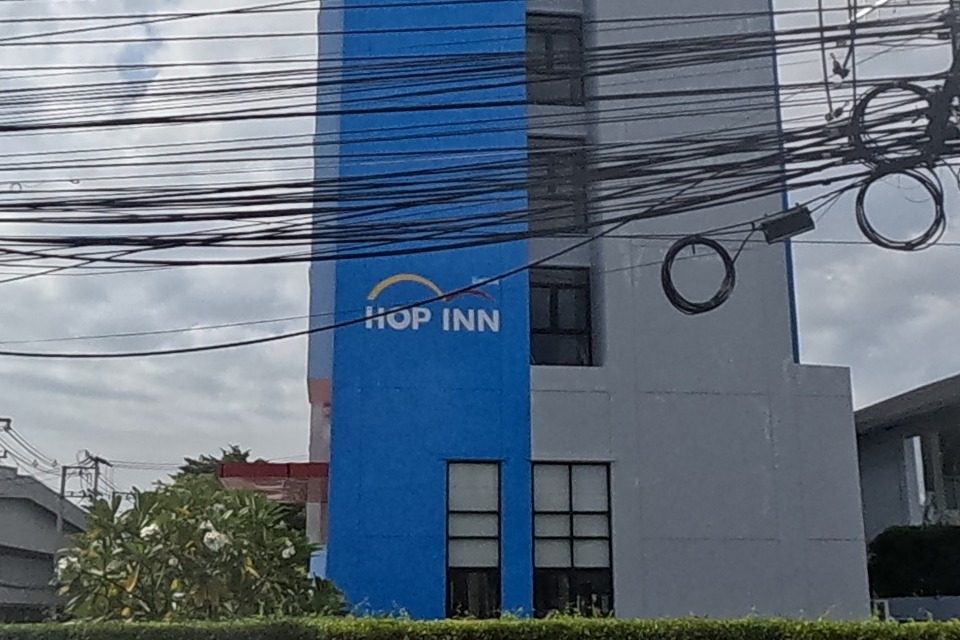 A blue-and-white 'Hop Inn' budget hotel tower, with an advertising board for 'Moose Bar & Restaurant' on the pole in front.