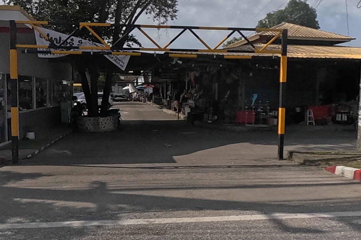 The entrance to a covered market lane lined with flower shops and stalls, buckets of flowers visible in a corner shop window; this is the Nim Si Seng flower market.