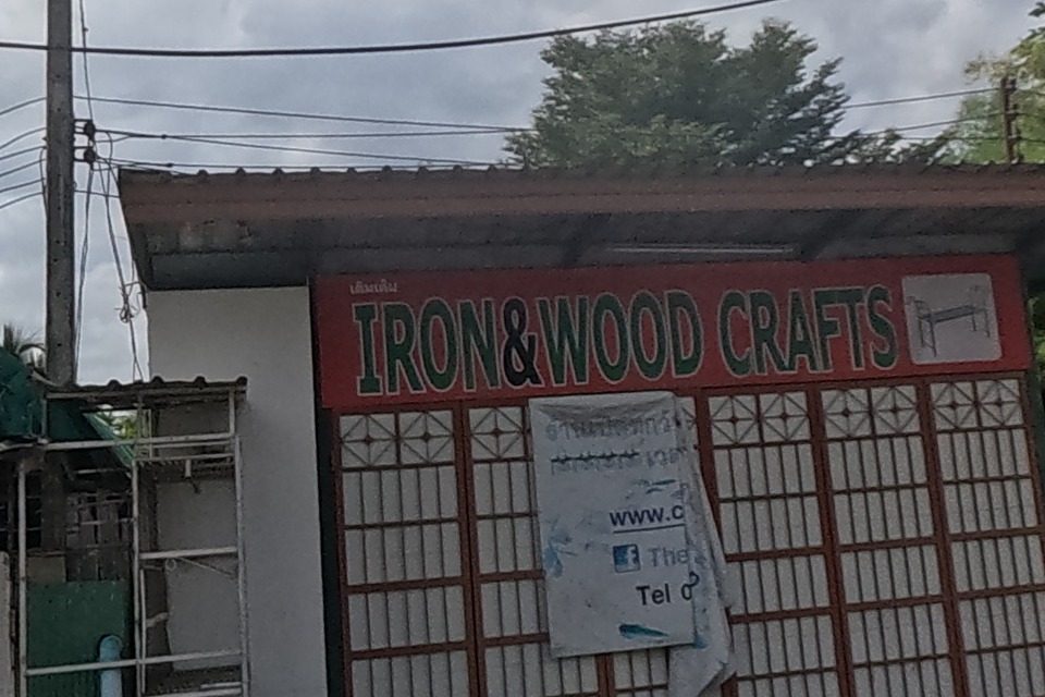 An 'Iron & Wood Crafts' shop with an ornate wrought-iron gate on display, next to a graffiti-covered fence.