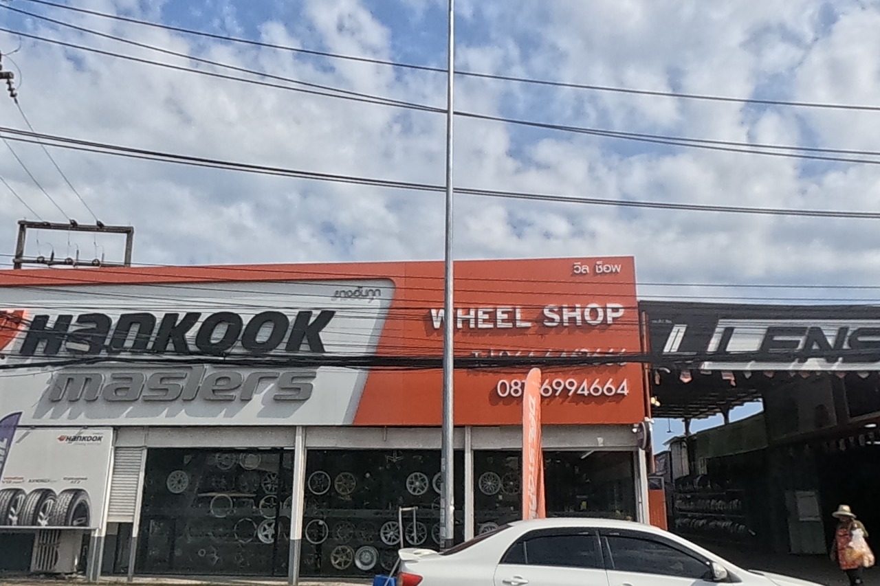 An orange-fronted wheel and tyre shop, Hankook Masters Wheel Shop, sits beside a Lenso wheel dealer and a Bridgestone sign, tyre price banners out front.