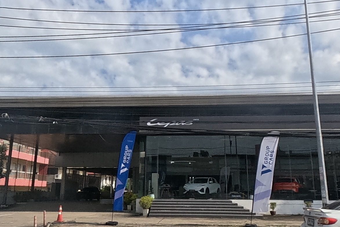 A Lexus showroom with V Group Cars flags displays cars behind glass, a large pink billboard with a phone number above.