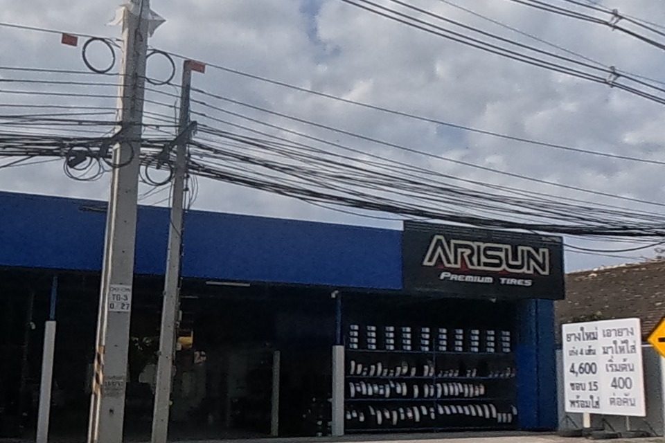 A blue-fronted Arisun Premium Tires shop displays a rack of new tyres beside a hand-lettered price board.