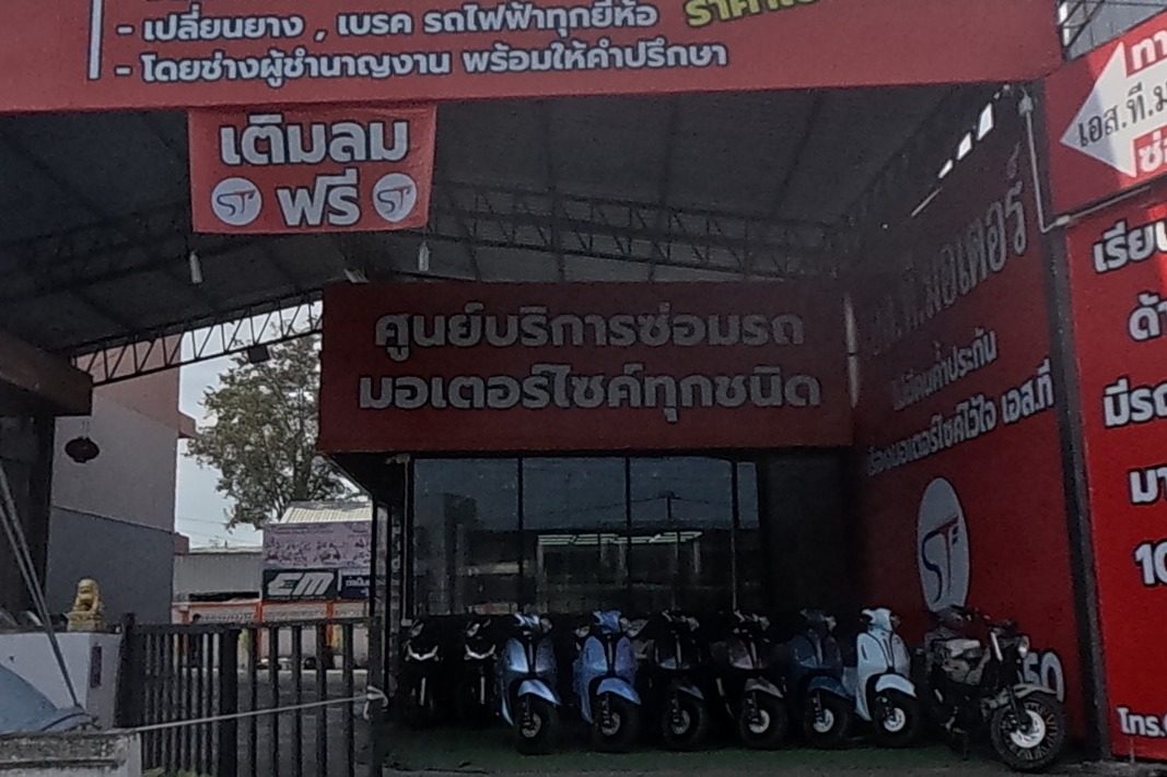 S.T. Motor, a motorbike sales and repair centre, displays rows of scooters for sale under a red awning with promotional banners for a 199-baht service, tyres from 350 baht, and a phone number.
