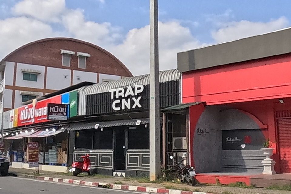 Across the road, the same corner shows TRAP CNX bar next to a red-fronted shop and, further along, the หมิงยู่พลาสติก plastics store.