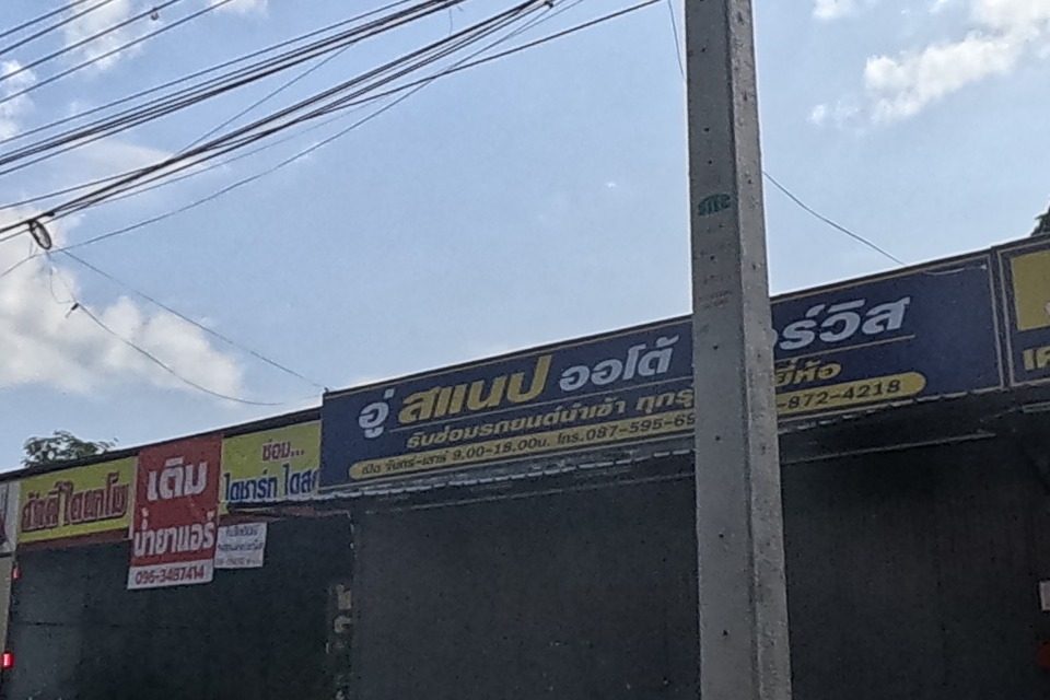 A row of shuttered repair shops: an imported-car garage, a general repair shop offering hybrid/AC/oil-change work, and small signs for AC gas refill and dynamo/starter repair.
