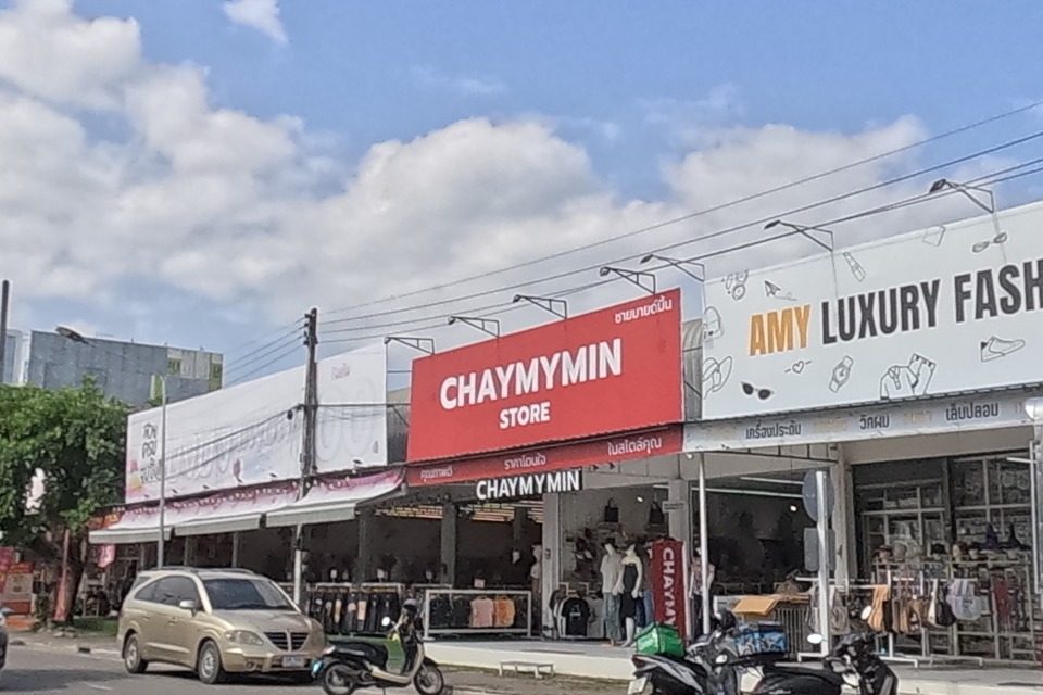 Across the road, CHAYMYMIN STORE and AMY LUXURY FASHION sit side by side, both clothing shops with scooters parked out front.