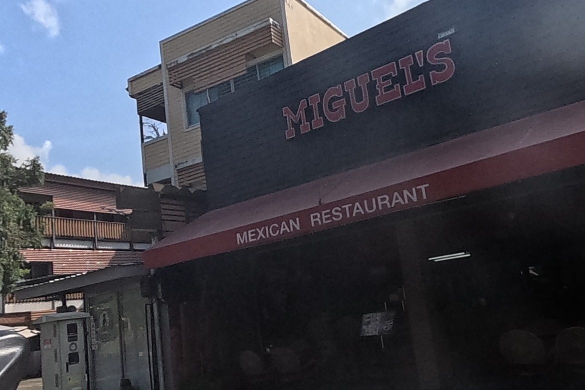 Miguel's Mexican Restaurant on the corner, roller shutters mostly down in the morning shadow, next to a gated orange-walled house.