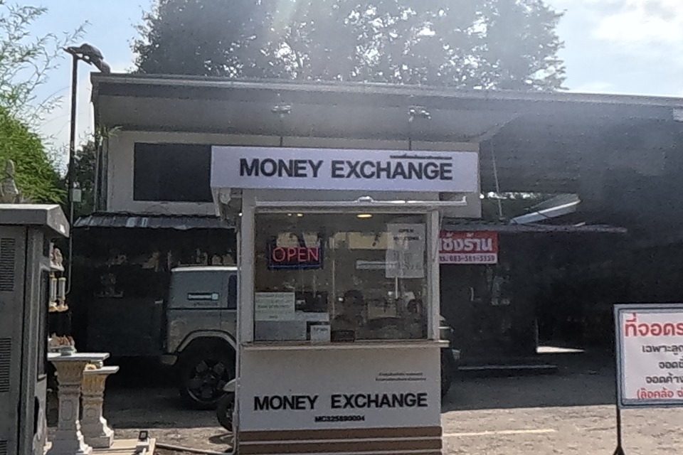 A parking lot in front of a condo building with a Money Exchange kiosk (open) and signs for a numbered Blue Coffee parking spot and a private paid parking lot.