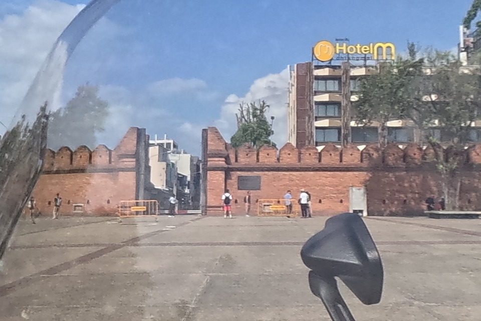 Across the road, the reconstructed brick city wall and arched gate of Tha Phae Gate stand behind an open plaza.