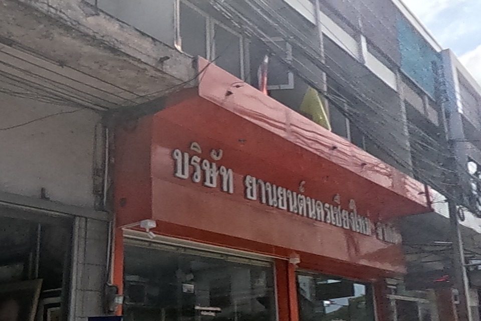 A company signed 'Yarn Yon Nakorn Chiang Mai' occupies a red-fronted shopfront with a picture-framing sign beside it; the road ahead has light traffic including a red songthaew and a scooter.